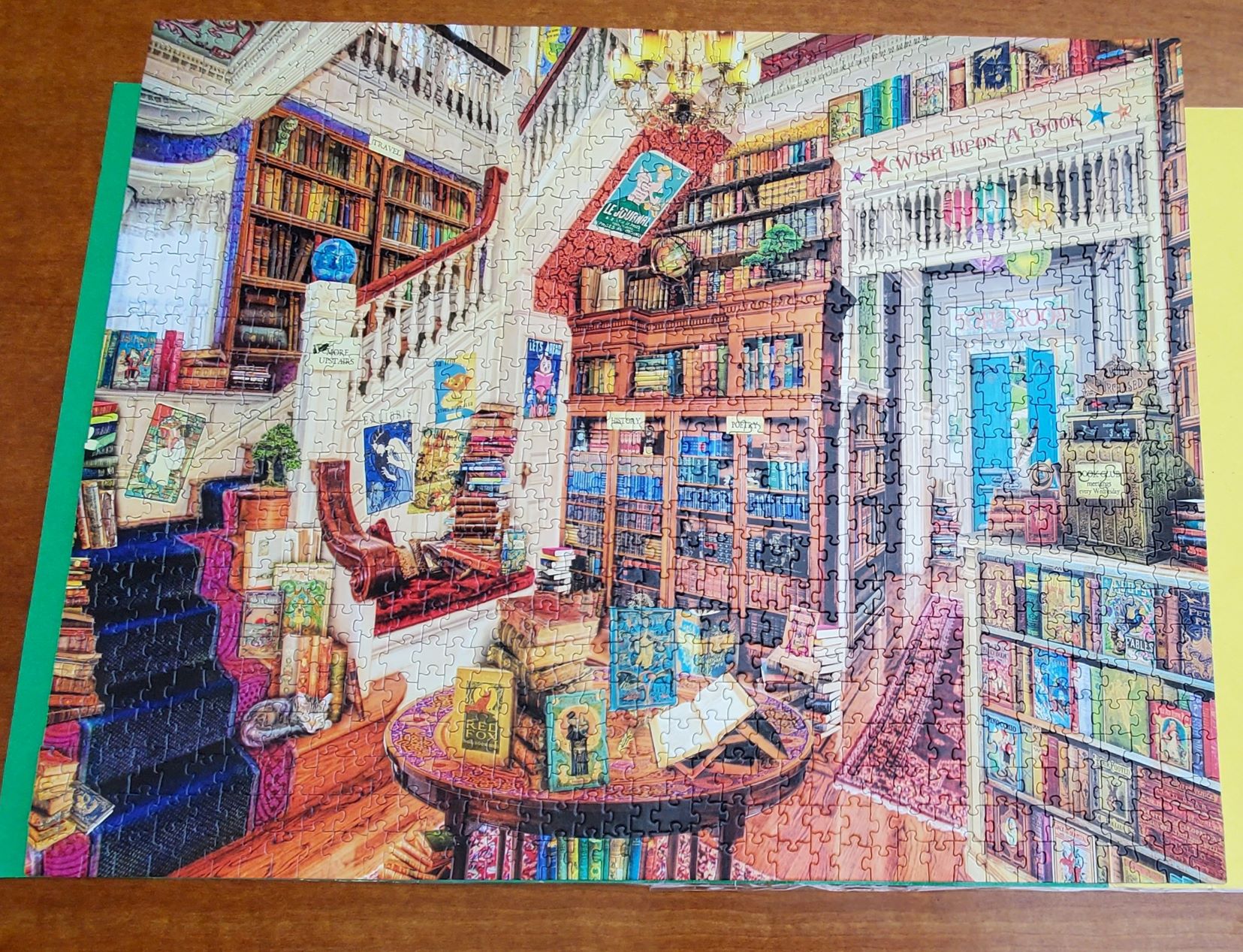 Completed jigsaw puzzle of interior of bookstore with books on shelves, tables, and stairs. There are cats hidden among the books.