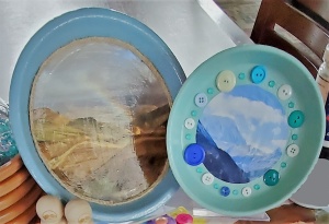 Two terra cotta dishes, painted blue and green, decorated with landscape photos and buttons